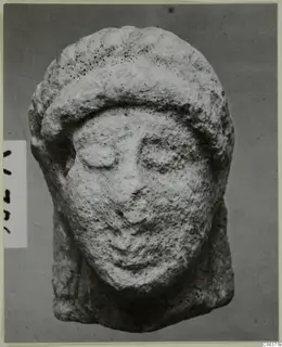 Limestone head from Vouni, seen from the front, with a band across the forehead and a pitted surface.