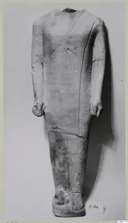 Headless limestone standing statue with arms held at its sides, shown against a plain grey background.