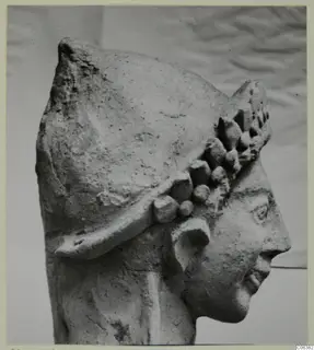 Terracotta head of a statue in profile facing right, with a helmet-like headdress studded with rounded knobs