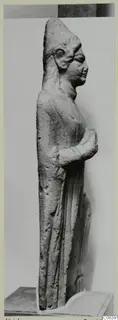 Limestone standing figure from Vouni, seen in profile on a plinth against a plain grey backdrop.