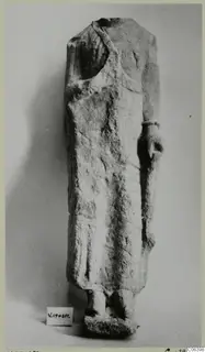 Limestone statue of a standing figure in a long garment, head and shoulders broken away, from Vouni, against a plain grey background.