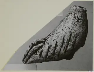 Curved limestone fragment with parallel incised grooves, a minor plastic find.