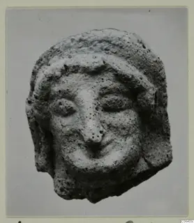 Small head of a figure in terracotta, with a headband, large eyes, a prominent nose and a wide mouth