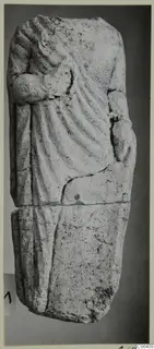 Limestone statue fragment of a draped standing figure, broken at the top and across the middle, shown upright.