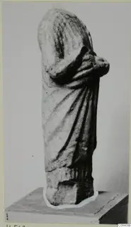 Limestone statue of a draped standing figure from Vouni, head missing, arms folded across the chest, shown on a plinth