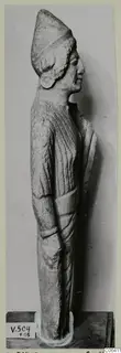 Limestone standing figure in side profile from Vouni, wearing a tall cap, shown on a dark base