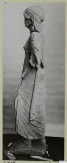 Side view of a limestone statue of a standing woman from Vouni, with a long draped garment and a rectangular base