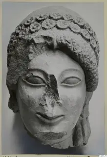 Front view of a limestone Kore statue head from Vouni, with a band of rosettes in the headdress and a broken nose.