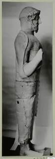Terracotta statue of a standing bearded man, seen in side profile on a dark base