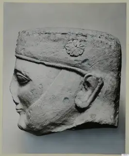 Limestone head fragment in profile facing left, with a flat headdress, rosette ornament and carved ear.