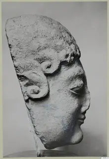 Limestone sculpture of a head from Arsos, with a high hair mass and spiral curls at the side.