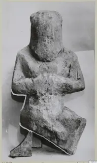 Limestone sculpture of a seated figure with arms folded across the body, head rounded and featureless