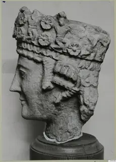 Carved limestone head in profile with a tall decorated headdress, on a wooden stand, from Vouni