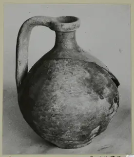Pottery juglet with a loop handle and round body, photographed against a grey backdrop.