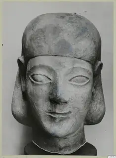 Limestone sculpture head with a flat-topped headdress, large ears and traces of blue paint, photographed from the front