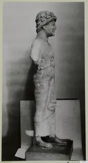 Limestone sculpture from Kition of a standing figure in profile, wearing a leafy wreath, arms missing at the shoulders