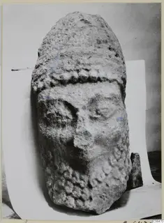 Limestone head from Kition, weathered face, standing upright on a white paper backdrop.