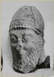 Limestone head from Kition, Oura S, with a tall headdress, a knobbed band across the brow and a worn face