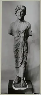 Limestone statue from Kition of a standing figure with a wreath-like headdress; arms broken off
