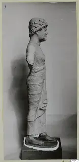 Limestone statue of a standing figure from Kition, seen in profile against a grey backdrop