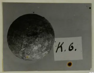 Round, pitted object photographed beside a small handwritten label card, Kition collection photograph
