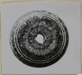 Disc-shaped stone object with a central hole and two raised concentric rings, shown on a mounted print