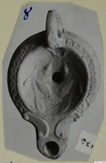 Terracotta oil lamp with a loop handle and a decorated rim, shown on a grey photo mount.
