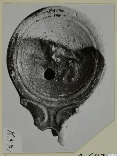 Terracotta lamp seen from above, with a central hole and a nozzle at the bottom edge
