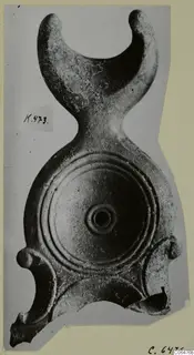 Terracotta lamp seen from above, with concentric grooves on its round disc and a crescent-shaped handle with two knobbed ends