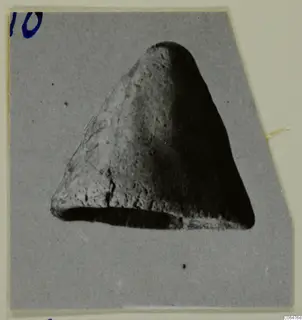 Terracotta object (K.462) with a rounded top, a flat lower edge and a pitted, rough surface, shown on a grey card