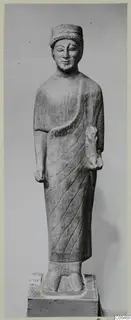 Limestone statue of a standing male figure in a cap and draped cloak, on a wooden base, from Vouni
