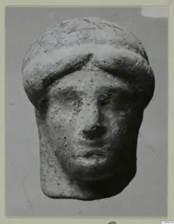 Small terracotta head of a figure with a rounded cap, face frontal, photographed against a grey backdrop