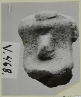 Terracotta figurine fragment with a blocky body and a rounded projection at the centre, shown on a grey card mount beside a number label