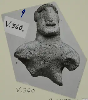 Terracotta figurine of a head and upper body with a broad face, shown in a photograph mounted on card