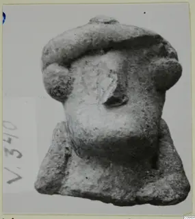 Small terracotta figurine fragment with a wide flat-topped headdress and projecting side knobs, photographed on a mounted card.