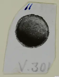 Small round find shown in a photograph mounted on a pale card, with a handwritten label and blue ink mark