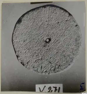 Round flat stone disc with a small central hole, photographed from above against a grey backdrop.
