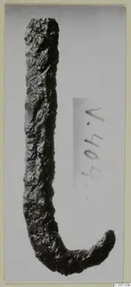 Corroded iron hook with a long straight shank and a short curved end, photographed against a grey background