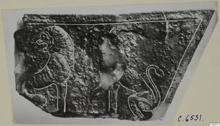 Corroded metal relief fragment with figures outlined in white paint, shown as a photograph on a light card mount