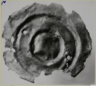 Corroded bronze disc fragment with concentric raised rings and two small holes, from Vouni.