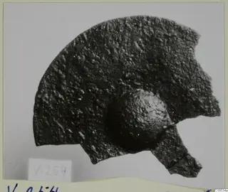 Corroded bronze mounting fragment from Vouni with a rounded knob, photographed on a pale ground.
