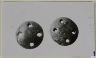 Two round stone objects, each pierced with several holes, shown side by side on a pale card