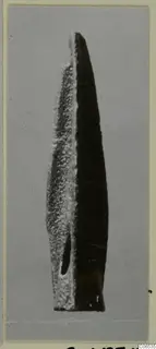 Long pointed metal blade, probably a weapon, with an oval hole near its base, shown upright on a grey backdrop.