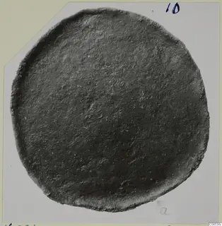 Disc-shaped bronze fragment from Vouni with a raised rim and dark, corroded surface