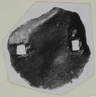 Corroded bronze mounting fragment from Vouni with two square openings, shown on a pale card mount