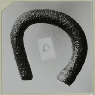 Bent metal rod in a U-shape with a dark, pitted surface, photographed on a pale grey background