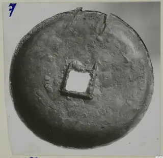 Round metal disc with a square central opening framed by a square metal mount, cracked at the top edge