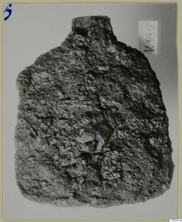 Corroded iron tool, possibly a spade, from Vouni, shown upright against a pale grey background.