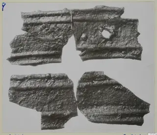 Four fragments of corroded bronze mountings with parallel raised ridges, one with a round hole, on a pale background