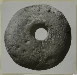 Disc-shaped object with a large central hole, grey-brown with a rough, pitted surface, from Vouni